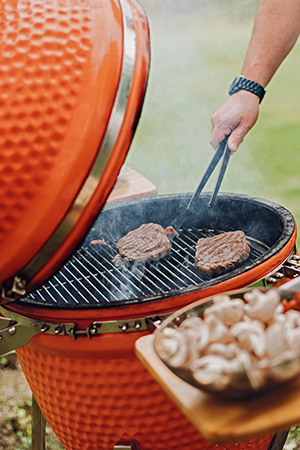 Jemand dreht auf einem roten Kugelgrill ein Stück Fleisch um